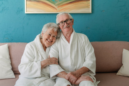 Happy senior couple sitting together in bathrobe on sofa, having nice time at home.の写真素材