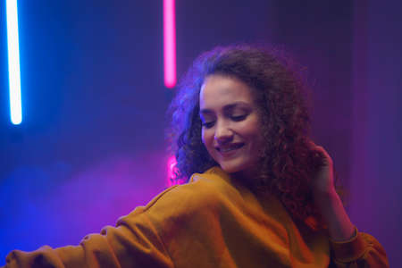 Portrait of a happy young woman dancing over neon light background at disco party