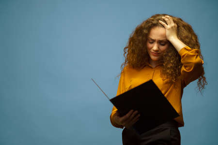 Studio portrait of worried businesswoman holding folder and papers, on grey background.の写真素材