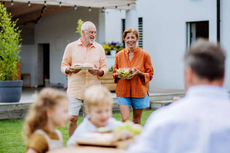 Happy senior couple bringing salad and burgers at multi generation garden party in summer.の写真素材