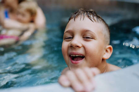 Little boy enjoying summer time in outdoor pool with his family, having fun.