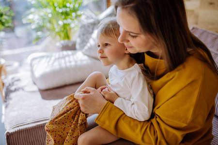 Young mother dressing up her little daughter in their home, moterhood concept.