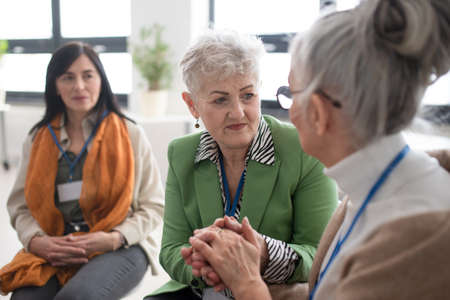 Group of senior people sitting in circle during therapy session, consoling depressed woman.の写真素材