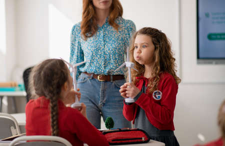 School girl holding model of wind turbine in front of classmates.