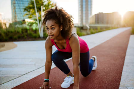 Young multiracial girl in sportswear preparing for run in city, during summer sunset, golden hour.