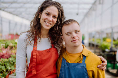Experienced woman florist posing with young colleague with Down syndrome in garden centre.の写真素材