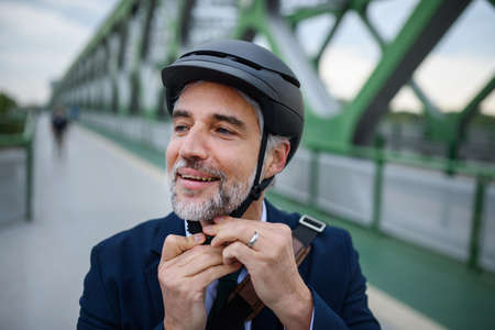 Portrait of businessman commuter on the way to work putting on cycling helmet, sustainable lifestyle...