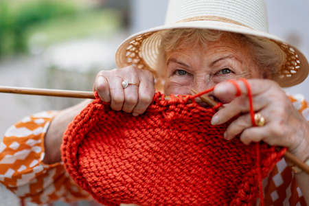 Portrait of senior woman sitting outdoor and knitting red scarf.の写真素材
