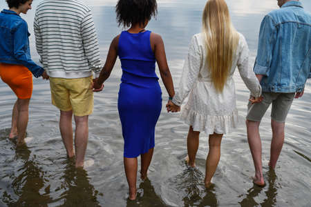 Multiracial group of young friends holding hands and standing in lake in summer. Rear view, high angle view.の写真素材
