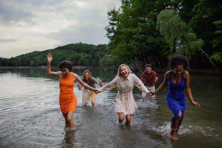 Multiracial group of young friends holding hands,standing in lake in summer and having fun.の写真素材