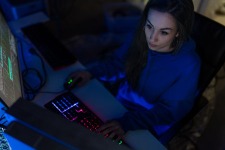 Young woman hacker by computer in the dark room at night, cyberwar concept.