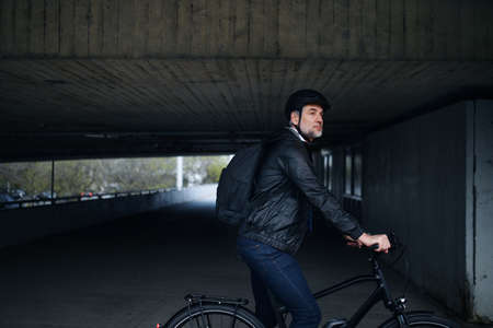 Businessman commuter on the way to work, riding bike under overpass, sustainable lifestyle concept. Dark background.の写真素材