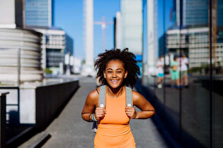 Multiracial teenage girl walking with backpack in modern city centre during summer day, back to school concept.の写真素材