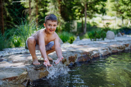 Funny little boy coming out from garden pond with splashing around him. Summer holiday, vacation concept.の写真素材