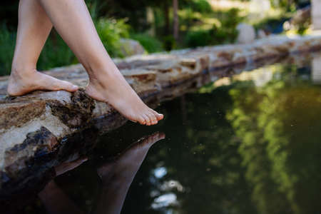 Unrecognizable young woman is dipping her foot in cool water of pond, refreshing and hardening concept.の写真素材