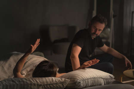 Upset mid adult woman with her husband in bed arguing, relationship problems concept.