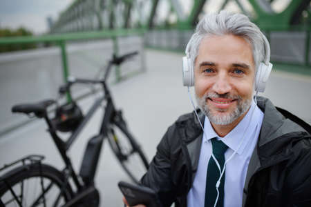 Businessman with bike sitting on bench, listening to music with feet up and resting. Commuting and...