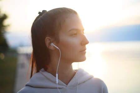 Young beautiful sportive girl listening to music at sunrise by the lake.の写真素材