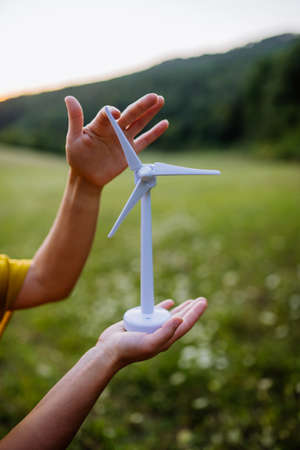 Close up of hands holding model of wind turibe in nature. Concept of ecology future and renewable resources.の写真素材