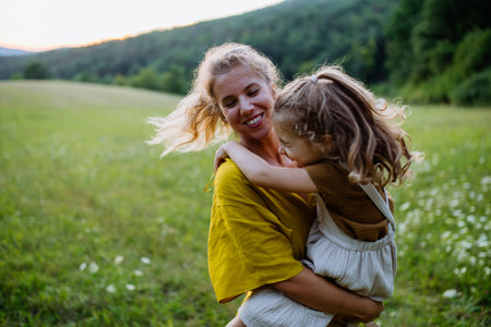 Happy mother spending time with her little daughter outside in green nature.