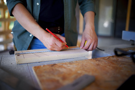 Carpenter measuring wooden planks and making marks with pencil, diy eco-friendly homes concept.