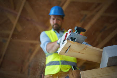 Low angle view of handyman working with circular saw on wooden construction site, diy eco-friendly homes concept.の写真素材