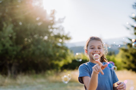Little girl having fun while blowing soap bubbles on a summer day in nature.の写真素材