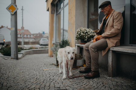Unhappy senior man sitting on bench in front of store and waiting somebody wih his big white dog.