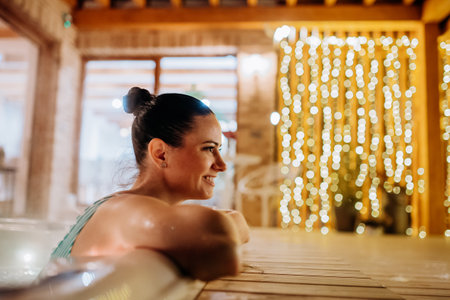 Young woman enjoying outdoor bathtub in her terrace during cold winter evening.