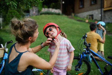 Young mother with little daughter preaparing for bike ride, putting on helmets.の写真素材