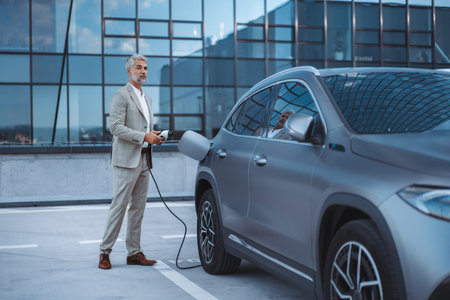 Businessman holding power supply cable at electric vehicle charging station.の写真素材
