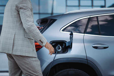 Man holding smartphone while charging car at electric vehicle charging station, closeup.の写真素材