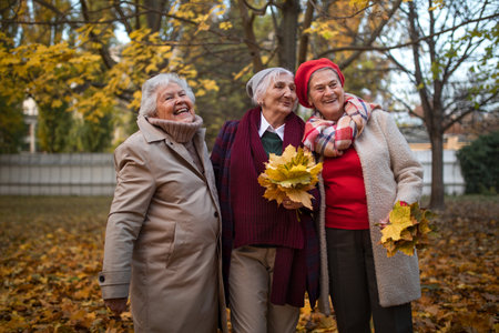 Happy senior female friends on walk outdoors in park in autumn day, having fun and throwing...