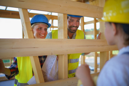 Happy family in protective clothes checking their unfinished eco wooden house, concept of...