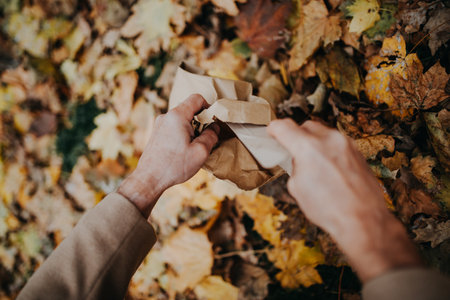 Close-up of dog owner picking excrements in paper bag during walking in autumn citypark.の写真素材