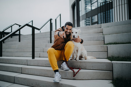 Portrait of happy young man and his dog outdoors in city staircase, looking at camera.