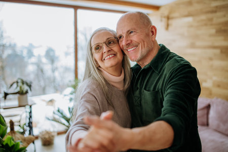 Senior couple in love dancing together in their modern living room.の写真素材