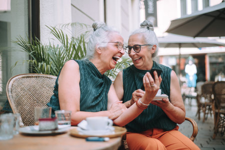 Happy senior women twins having coffee break in city, smiling and talking.の写真素材