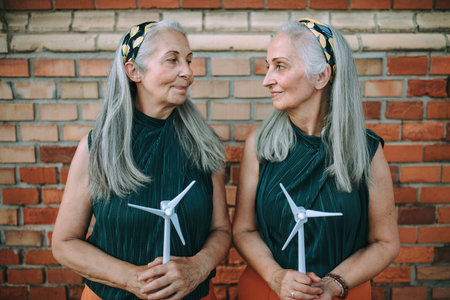 Senior women, twins holding plastic model of wind turbine, concept of future, ecology and renewable...