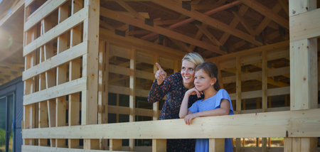 Mother and daughter on site inside new ecology wooden home construction framing looking at view.の写真素材
