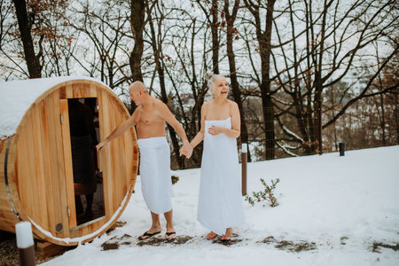 Senior woman in towel with her husband entering to outdoor sauna during cold winter day.の写真素材