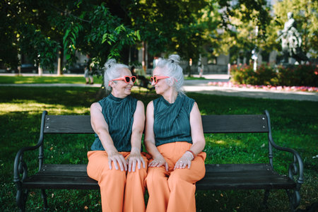 Happy senior sister, twins sitting in city park and resting after shopping.の写真素材