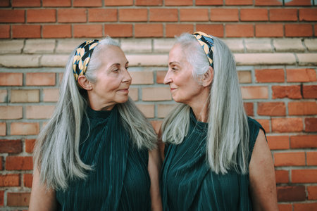 Portrait of senior women, twins,in same clothes standing back to back, outdoor in city.の写真素材