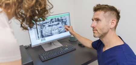Young dentist showing x-ray scan at computer to his patient.