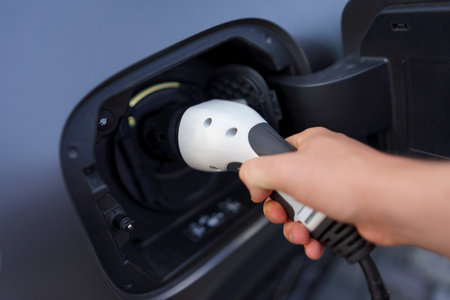 Man holding power supply cable at electric vehicle charging station, closeup