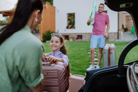 Happy family preparing for holiday, putting suitcases in car trunk, while their electric car charging.の写真素材