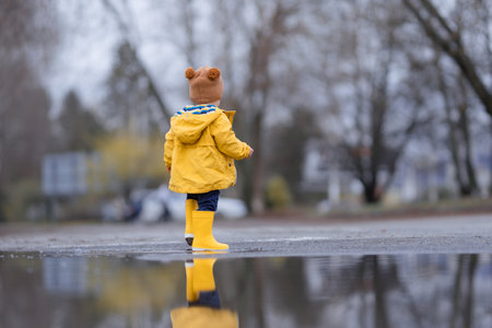 Happy little boy jumping in puddle after rain in autumn day.の写真素材