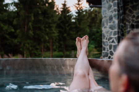 Unrecognizable young woman with feet up relaxing in hot tub outdoor in nature.の写真素材
