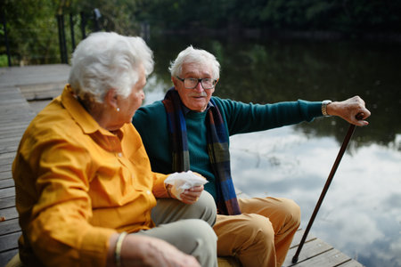 Happy senior couple in autumn clothes having break near lake after walk.の写真素材