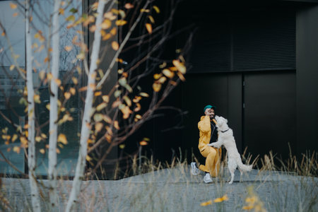Happy young man walking and training his dog outdoors in city during autumn day.